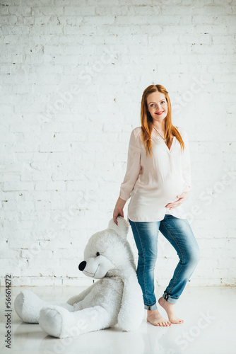 Fototapeta Naklejka Na Ścianę i Meble -  red-haired pregnant girl in a light blouse and blue jeans with a teddy bear