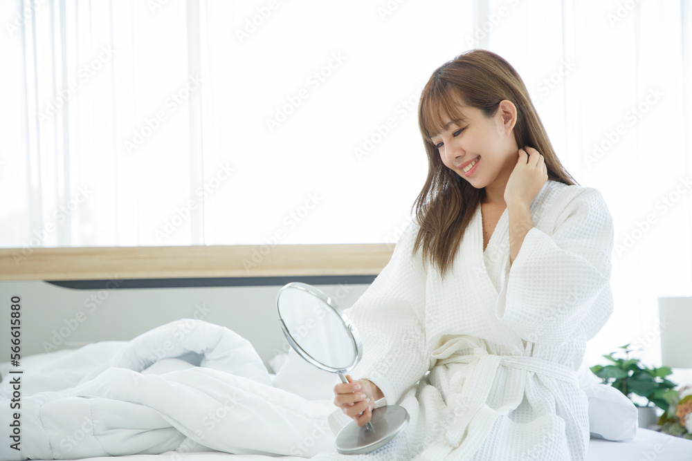 Woman sitting on the bed with the mirror after waking up, side view, entering a day happy and relaxed after good night sleep. Sweet dreams, good morning, new day, weekend, holidays concept. Woman sitting on the bed with the mirror after waking up, side view, entering a day happy and relaxed after good night sleep. Sweet dreams, good morning, new day, weekend, holidays concept.