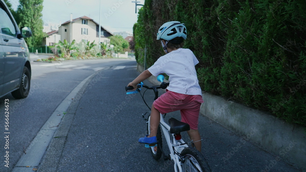 Obraz premium Little boy riding bicycle in city sidewalk. Child rides bike with wheels in street wearing helmet