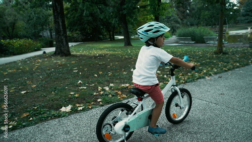 Fototapeta Naklejka Na Ścianę i Meble -  Child rides bicycle at park wearing protective helmet. Sportive child rideing bike with wheels outdoors. Active kid exercising