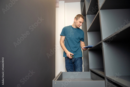 A young man takes measurements and collects shelves in the closet according to the instructions