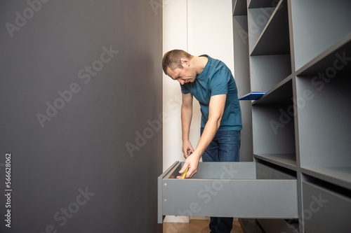 A young man collects furniture shelves in the closet according to the instructions
