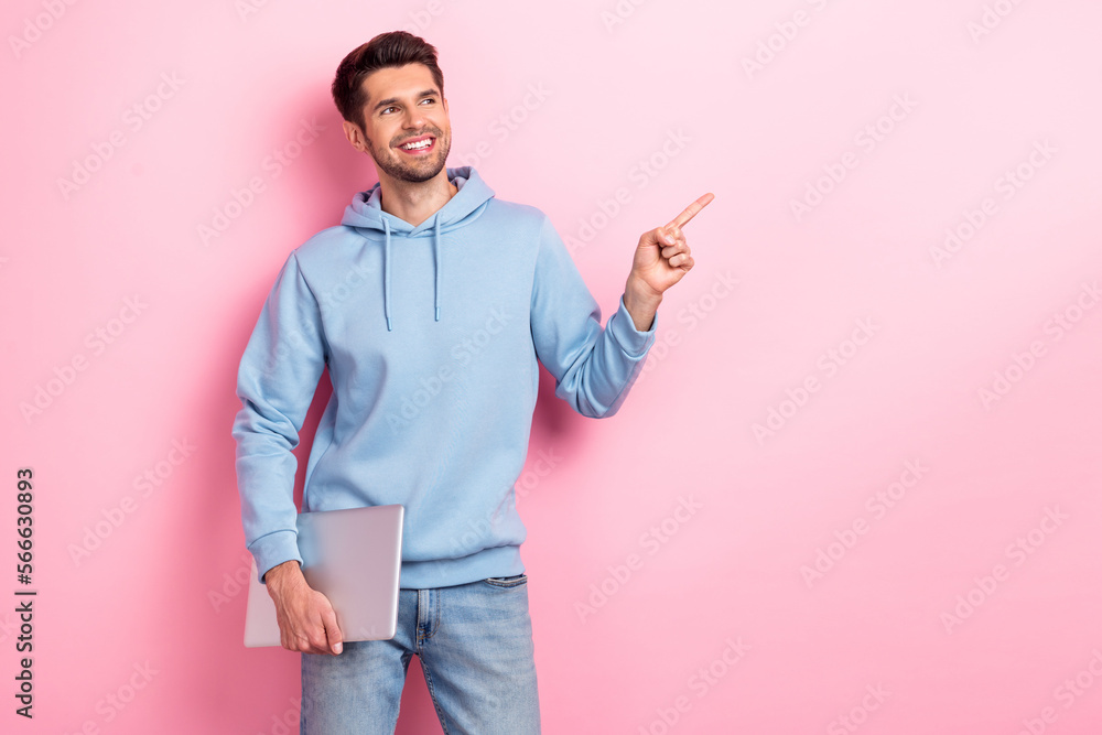 Photo of positive dreamy man wear blue hoodie holding modern device looking pointing empty space isolated pink color background Photo of positive dreamy man wear blue hoodie holding modern device looking pointing empty space isolated pink color background