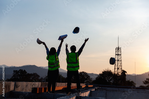 Silhouette image of engineer civil and construction worker throw up safety helmet and construction drawing against the background of surreal construction site in twilight or dark cityscape.