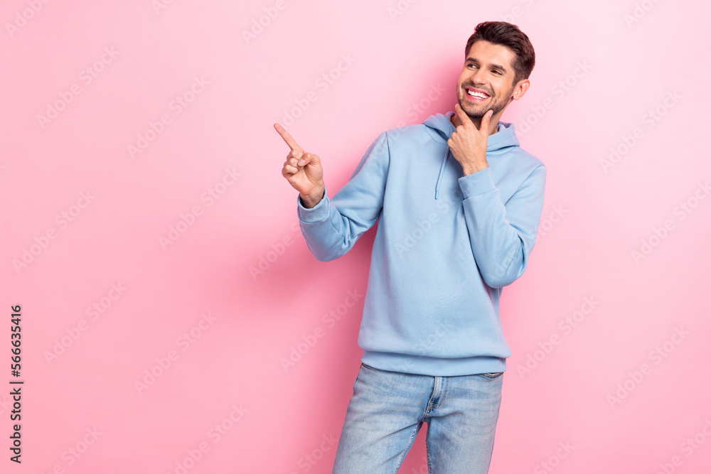 Photo of thoughtful charming man wear blue hoodie smiling arm chin looking pointing empty space isolated pink color background Photo of thoughtful charming man wear blue hoodie smiling arm chin looking pointing empty space isolated pink color background