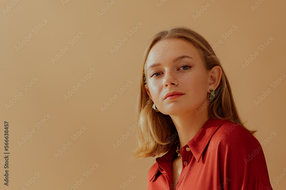 Fashionable confident blonde woman wearing elegant green hoop earrings, sating blouse, posing on beige background. Copy, empty space for text Fashionable confident blonde woman wearing elegant green hoop earrings, sating blouse, posing on beige background. Copy, empty space for text