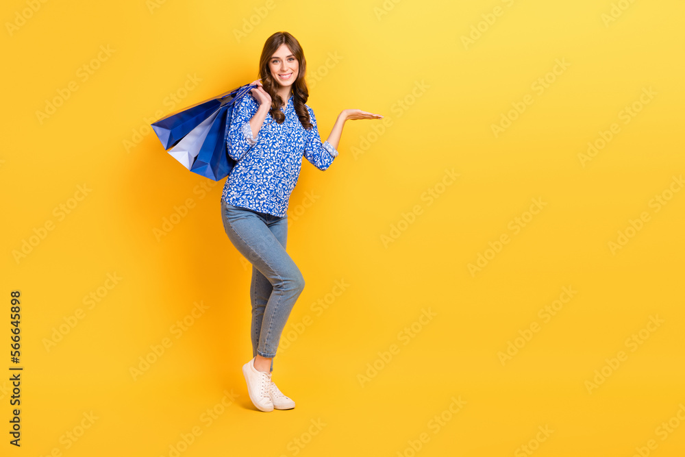 Full length portrait of cheerful person hold store bags hand hold demonstrate empty space isolated on yellow color background Full length portrait of cheerful person hold store bags hand hold demonstrate empty space isolated on yellow color background