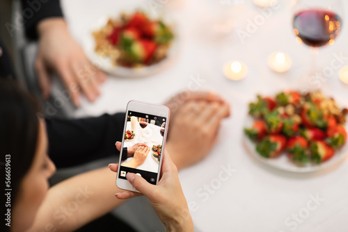 Female taking photo while holding her fiance hand, using smartphone