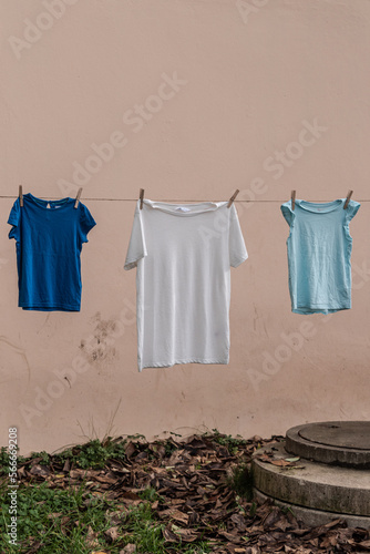 Three t-shirts on a thread held with wooden laundry pins against a plain orange background