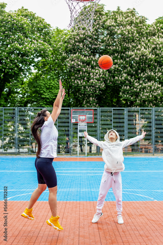 Girl and her younger brother, teenager, play basketball on modern basketball court under open sky