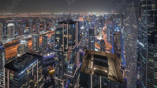 Panorama showing Dubai Marina and JLT district with traffic on highway between skyscrapers aerial night .