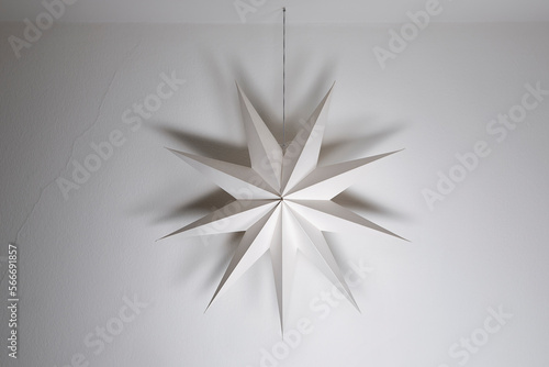 Obraz na płótnie Cardboard paper star hanging on a white wall background. Simple nordic style home festive geometric decoration, christmas, winter time. w salonie