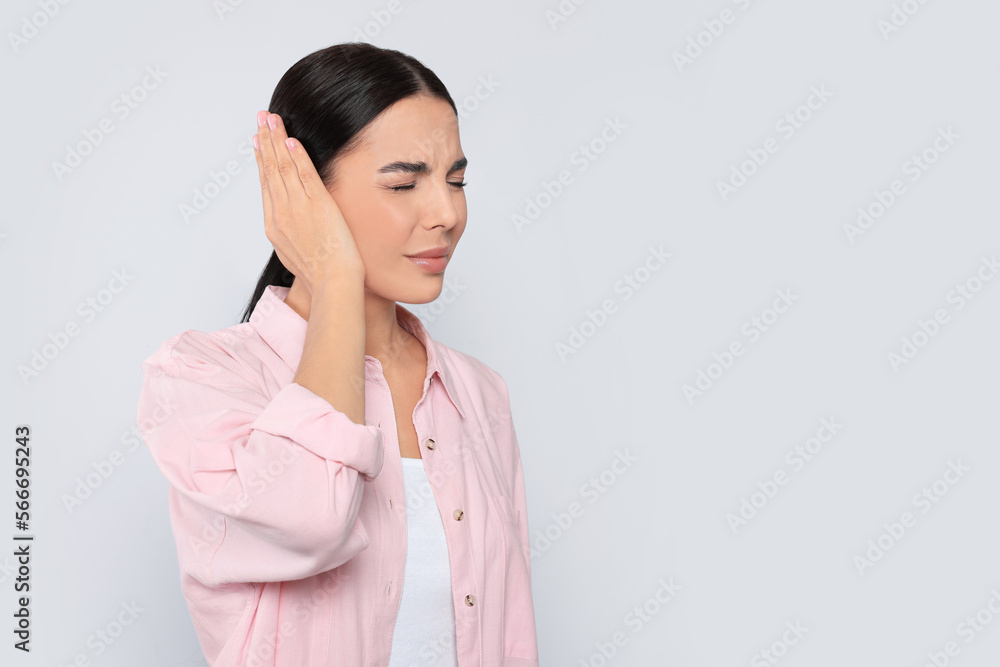 Young woman suffering from ear pain on light grey background. Space for text Young woman suffering from ear pain on light grey background. Space for text