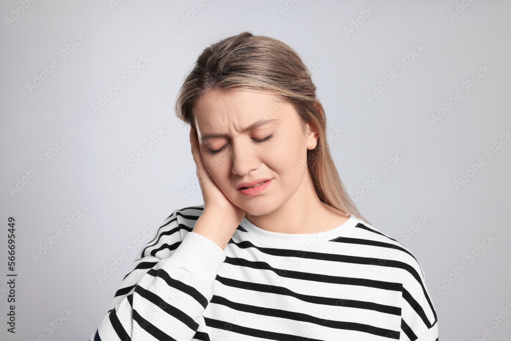 Young woman suffering from ear pain on light grey background Young woman suffering from ear pain on light grey background