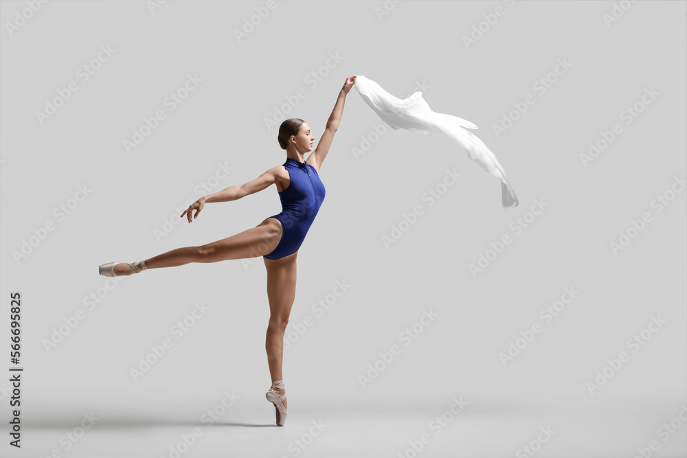 Graceful young ballerina practicing dance moves with veil on light grey background