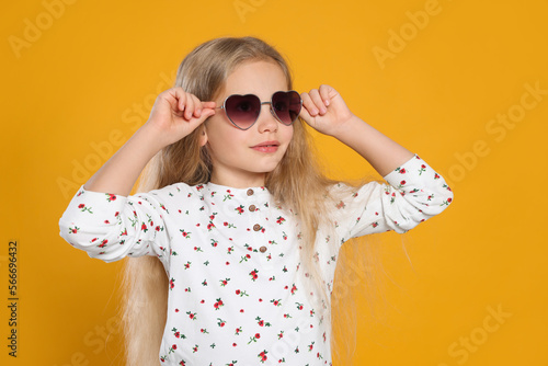 Girl wearing stylish sunglasses in shape of hearts on orange background