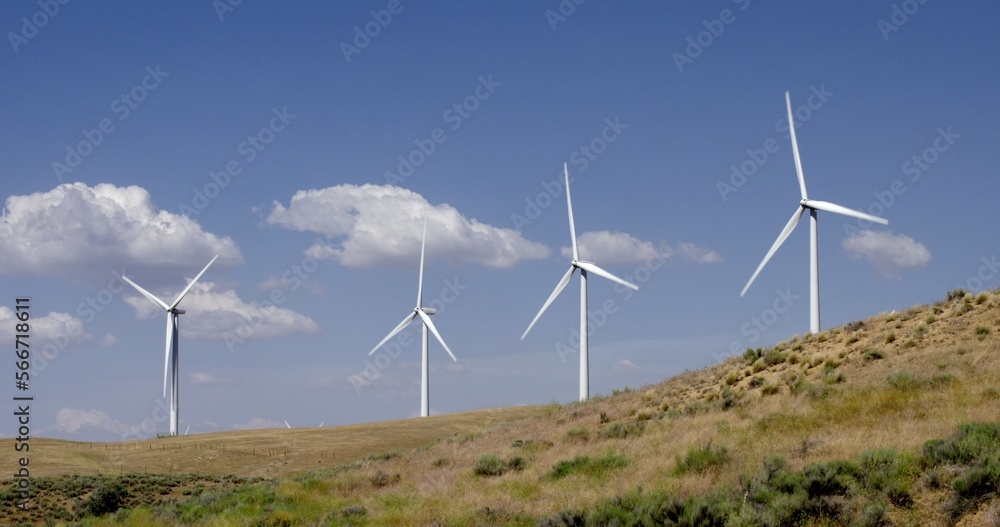 Large wind turbines operating on a rural hillside in the Tehachapi Mountains in California. Blue sky and puffy cumulus clouds behind them. Large wind turbines operating on a rural hillside in the Tehachapi Mountains in California. Blue sky and puffy cumulus clouds behind them.