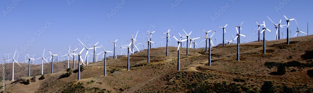 Wide view of lots of wind turbines generating power on a hillside at a wind farm near the Tehachapi Mountains in California. Clear blue sky. Wide view of lots of wind turbines generating power on a hillside at a wind farm near the Tehachapi Mountains in California. Clear blue sky.