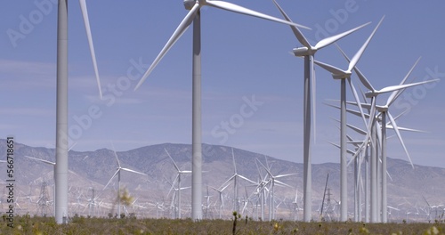Massive wind turbines generating power in heat haze on scrubby desert land at a wind farm near the Tehachapi Mountains in California.  Blue sky with a few clouds. photo