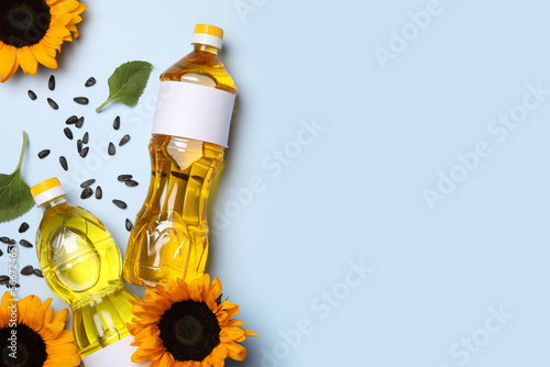 Bottles of sunflower cooking oil, seeds and beautiful flowers on light background, flat lay. Space for text