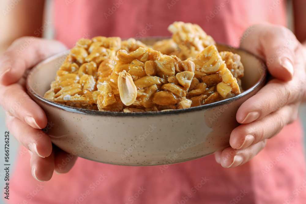 Woman holding bowl with delicious peanut kozinaki bars, closeup Woman holding bowl with delicious peanut kozinaki bars, closeup