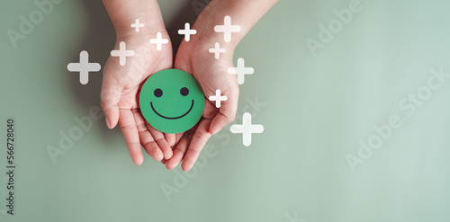 Hands holding green happy smile face, good feedback rating, positive customer review, experience, satisfaction survey, smiley mental health, child wellness, world mental health day on green background photo