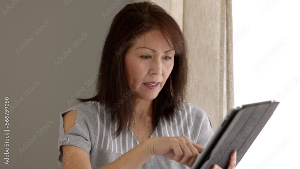 Attractive middle age woman relaxing shopping online with tablet and e-commerce credit card excited with success sitting near window in natural leisure home living room Attractive middle age woman relaxing shopping online with tablet and e-commerce credit card excited with success sitting near window in natural leisure home living room