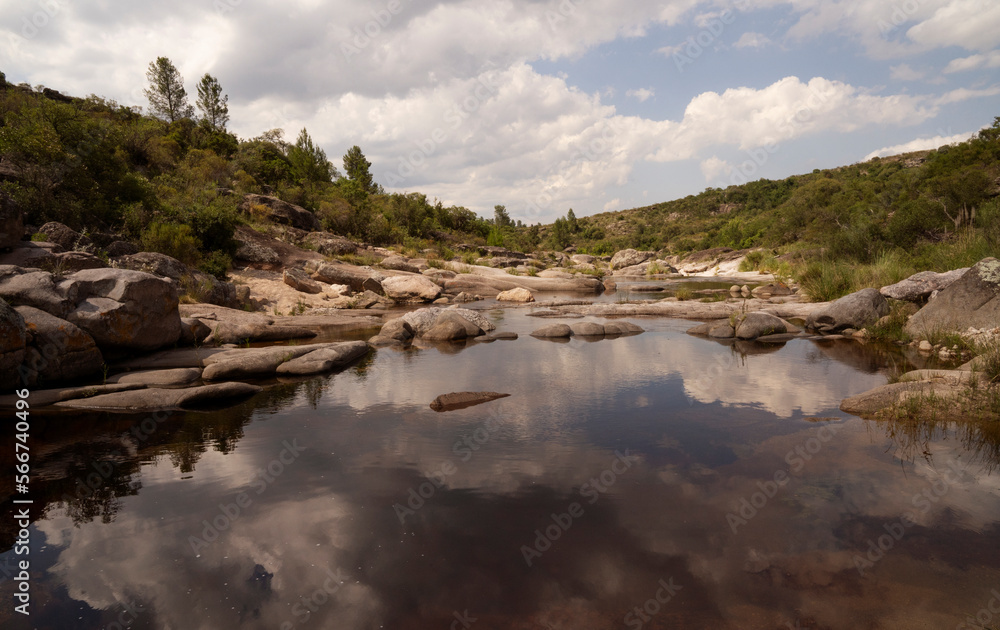 Serene view of the river flowing across the forest and rocky hills. Beautiful sky and clouds reflection in the water surface. 