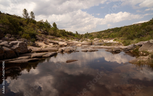 Serene view of the river flowing across the forest and rocky hills. Beautiful sky and clouds reflection in the water surface. 