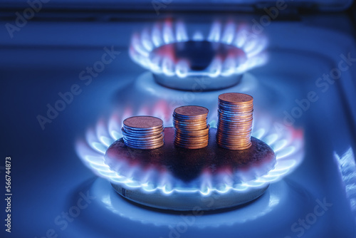 Gas stove lit, with stacks of coins above it. Increase in gas costs and tariffs. Gas stove with a burning fire and coins