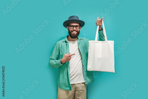 Young man is holding white textile eco bag on blue studio background. Mockup for design photo