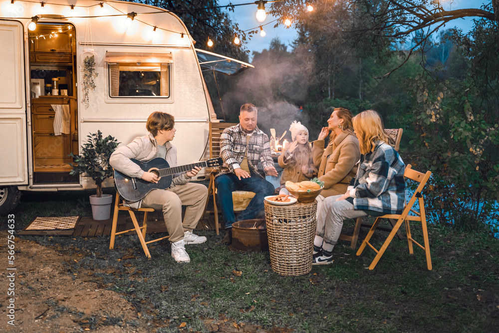 Family trailer travel.Children,brother sister,mom dad playing guitar,singing song at fire.Evening picnic in nature.Holiday barbecue BBQ food.Vacation weekend dinner.Road lunch.Camper,house on wheels Family trailer travel.Children,brother sister,mom dad playing guitar,singing song at fire.Evening picnic in nature.Holiday barbecue BBQ food.Vacation weekend dinner.Road lunch.Camper,house on wheels