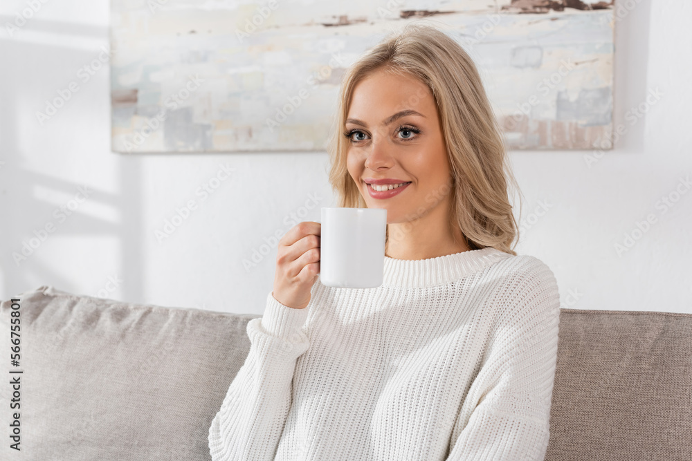 dreamy young woman in white sweater holding cup of coffee and smiling at home. dreamy young woman in white sweater holding cup of coffee and smiling at home.