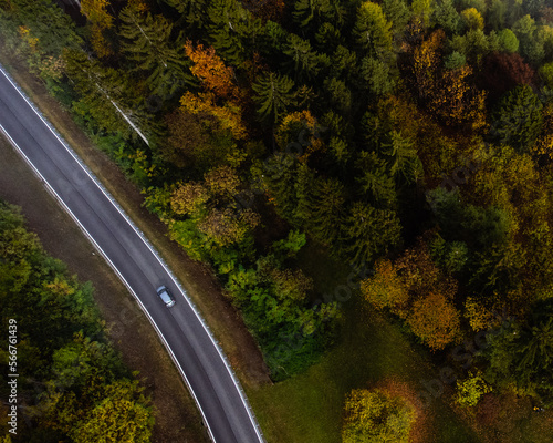 Road trip around Italy. Drone photo. Gray car on the beautiful autumn road. Wet asphalt circled by bright autumn forest.