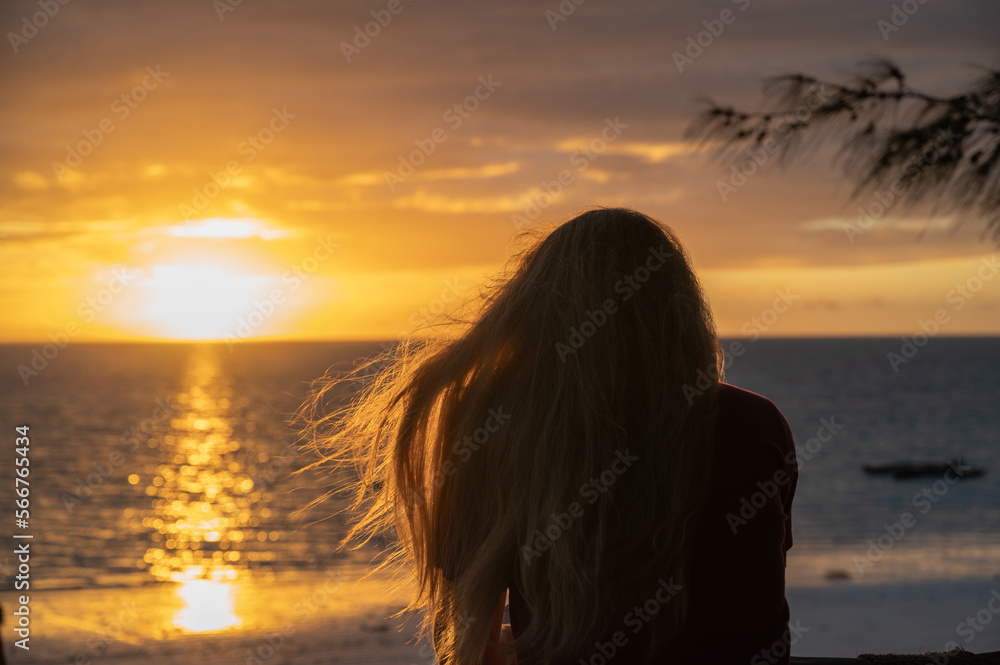 Young blonde girl from behind watching the sunrise on a beach in Zanzibar (Africa) Young blonde girl from behind watching the sunrise on a beach in Zanzibar (Africa)