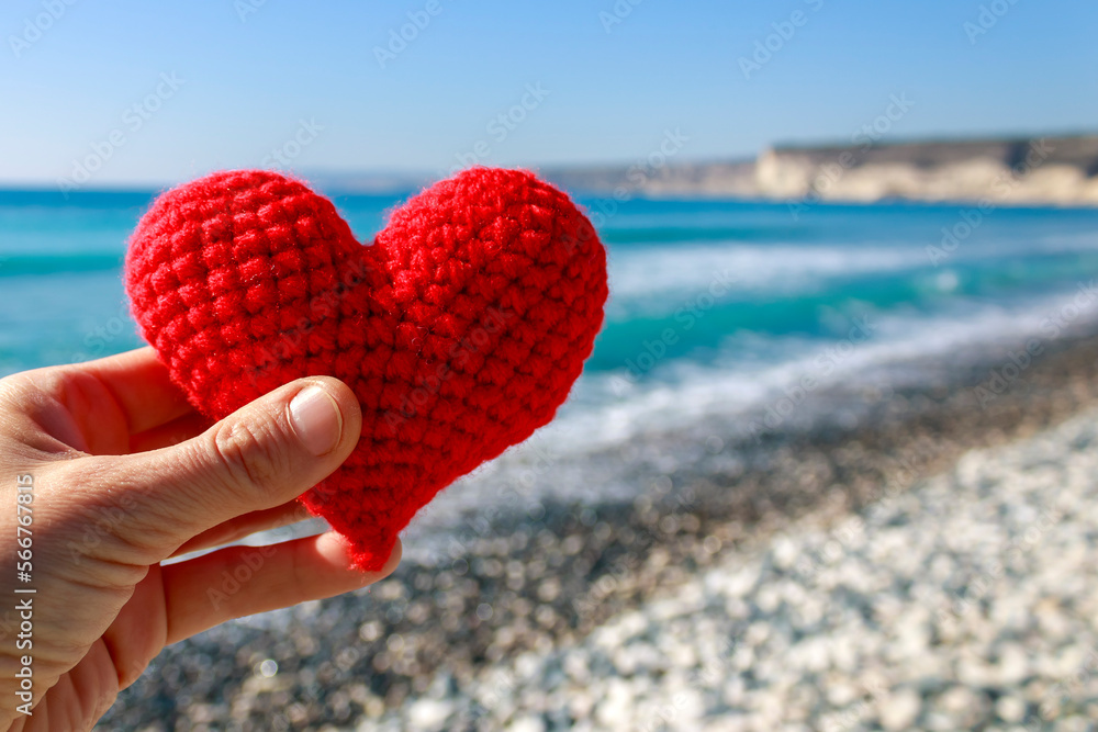 Fototapeta premium Close-up of red crochet heart in hand on sea beach