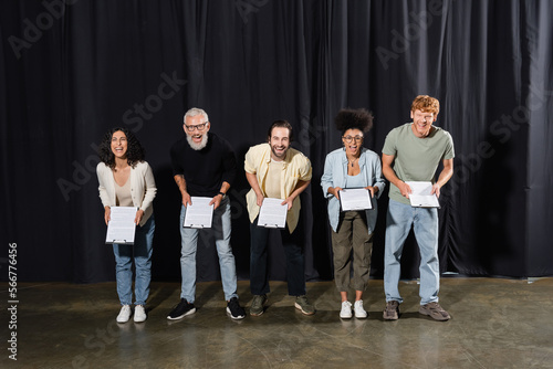 excited actors with bearded screenwriter looking at camera and laughing on stage in theater. photo