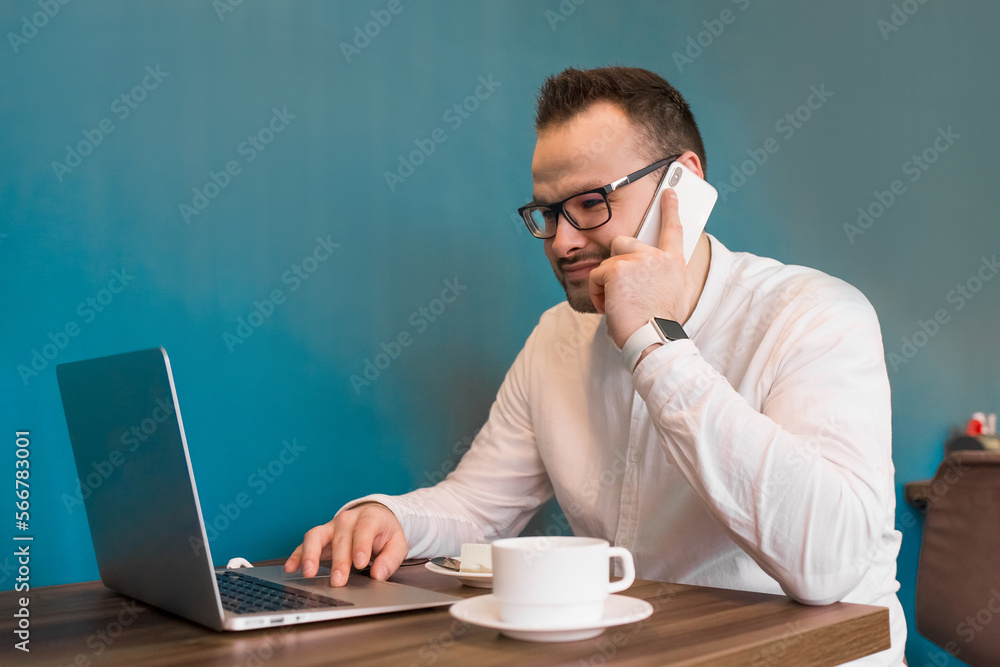 A fellow businessman in a white shirt sits at a desk in a laptop and talks on the phone for a coffee break A fellow businessman in a white shirt sits at a desk in a laptop and talks on the phone for a coffee break