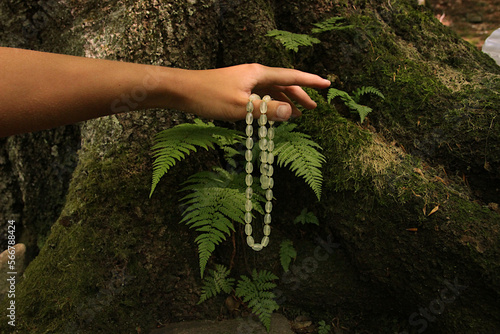 Green faceted beads made of grossular (pomegranate) in the hand opposite the fern bush.