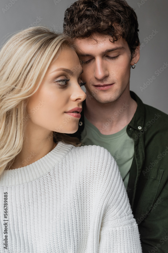 portrait of curly young man with closed eyes near blonde woman in white sweater.