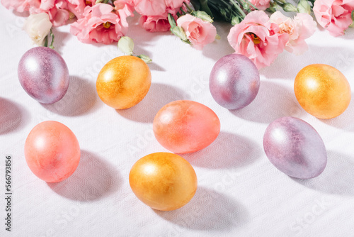 Gold, purple and pink painted Easter eggs in pastel colors and flower bouquet on a white cotton tablecloth