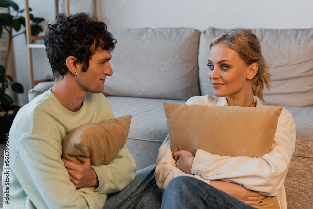 happy woman with blonde hair and curly man looking at each other while holding pillows. happy woman with blonde hair and curly man looking at each other while holding pillows.