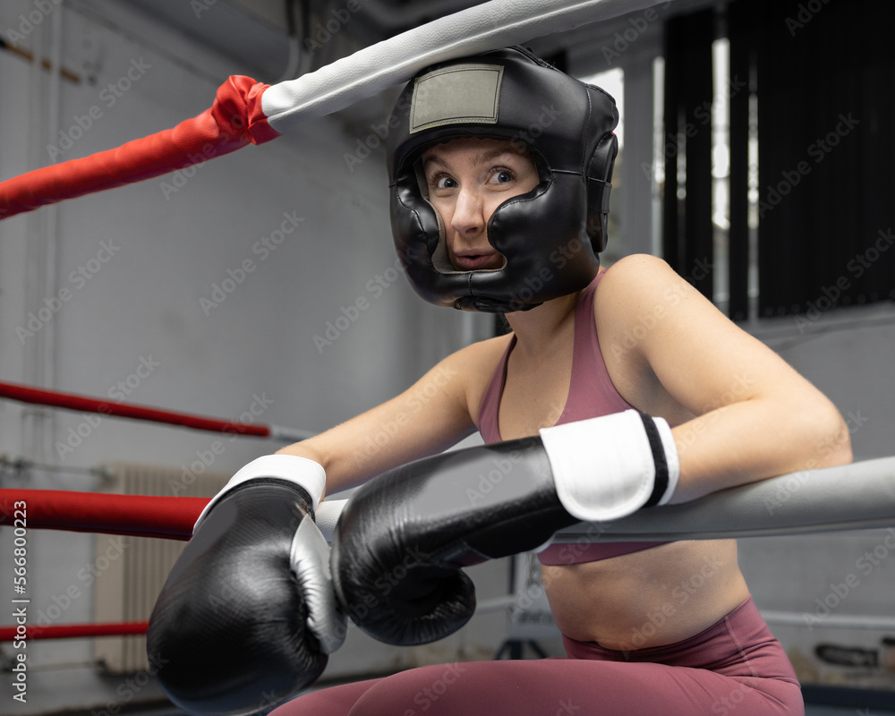 A young boxer girl sits in the ring, leaning against the fence. The concept of women's sport