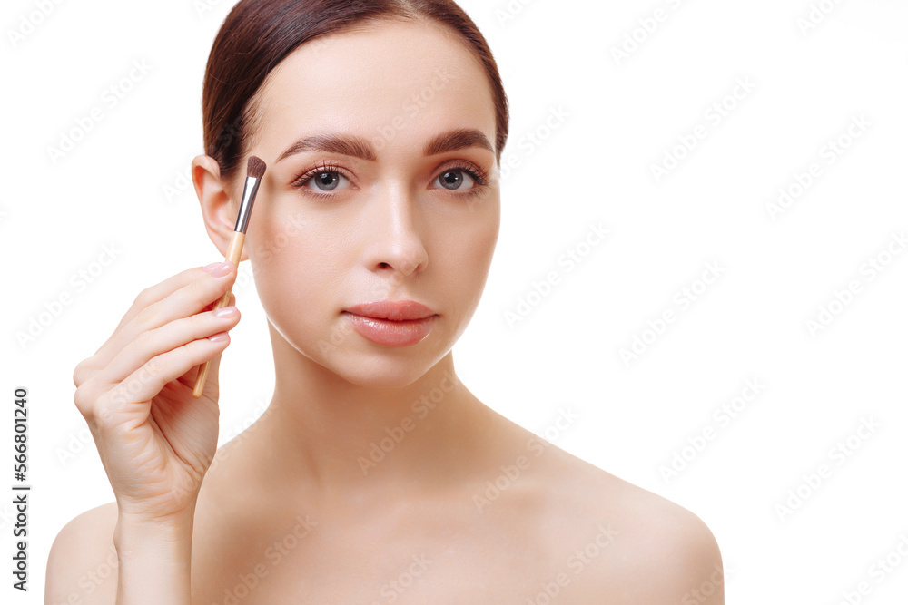 Portrait of an attractive young brunette woman, bare-shouldered, holding a cosmetic brush near her face on a white background. The concept of make-up, cosmetic procedures.