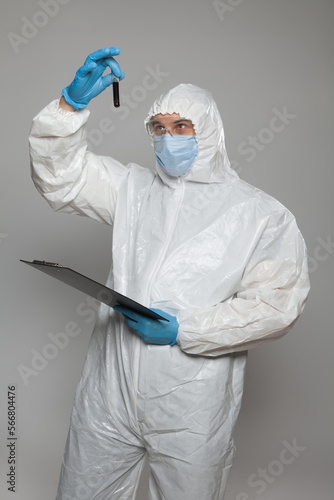Scientific virologist. Biologist in protective suit and blue gloves holds test tube with blood. Test tube with viruses concept. Virus University employee.