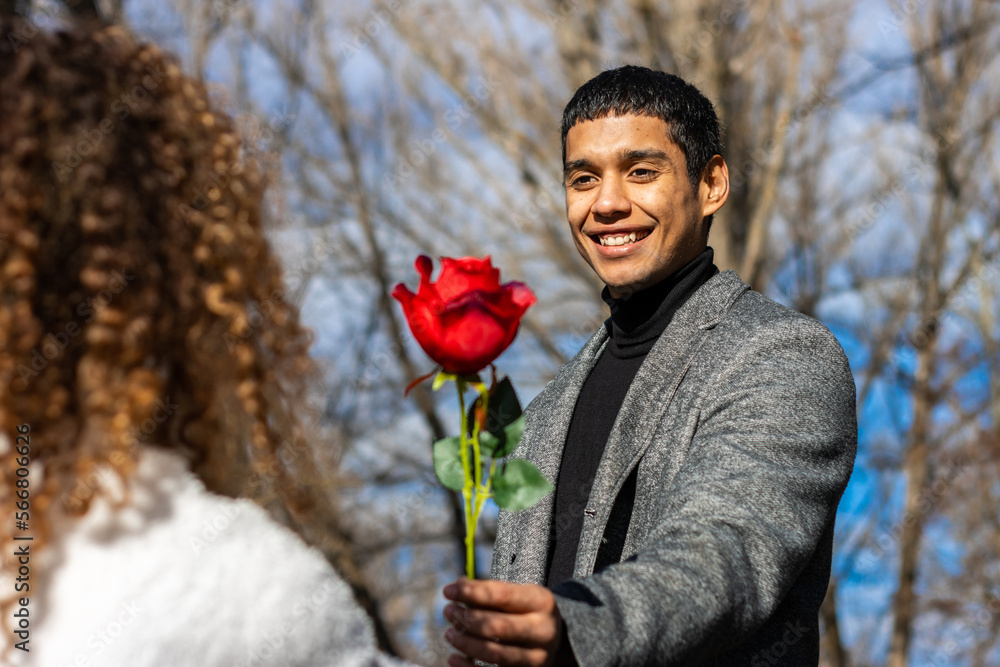 Man in love giving a rose to his girlfriend. Smiling guy in love giving a rose to his girlfriend outdoors Man in love giving a rose to his girlfriend. Smiling guy in love giving a rose to his girlfriend outdoors