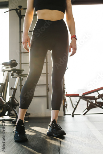 Cropped image of a female figure in tight black leggings on the gym. Vertical view.