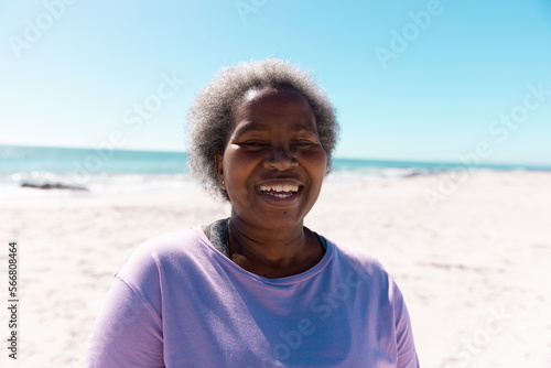 Happy african american senior woman with short gray hair smiling at sandy beach under clear blue sky