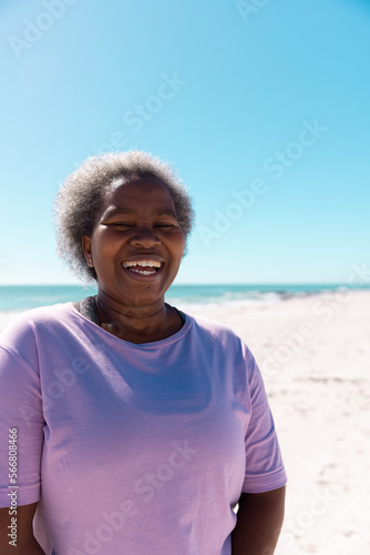 African american senior woman with short gray hair laughing at beach against clear sky on sunny day
