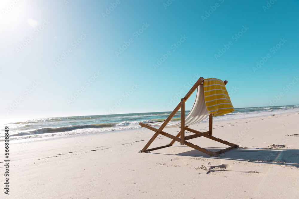 Empty deckchair with yellow napkin on sandy beach under clear blue sky during sunny day